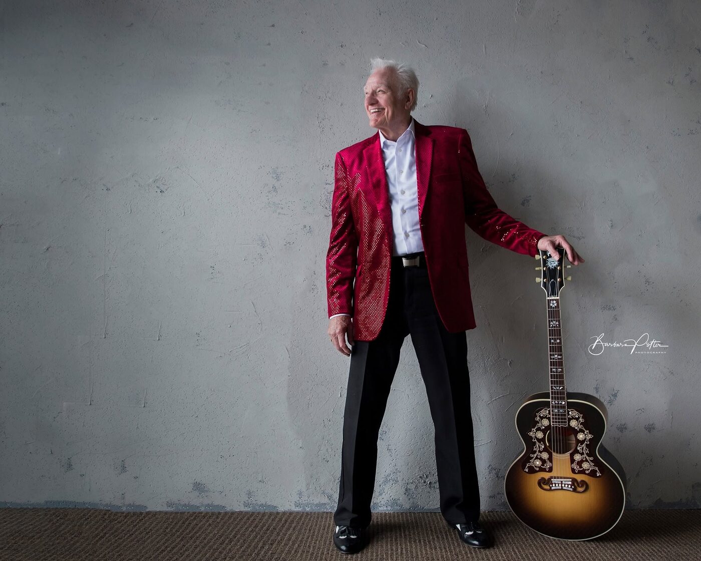 Jerry Foster in a red jacket standing with his acoustic guitar